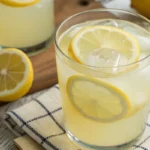 Close-up of a glass of healthy lemonade with lemon slices, served on a bright white background with natural lighting.