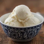 Three scoops of creamy homemade coconut ice cream in a blue bowl, showcasing its smooth, delicious texture.