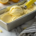 Delicious homemade lemon ice cream in a metal pan with a scoop, perfect for a refreshing treat.
