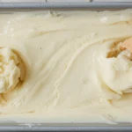 Close-up of homemade pineapple coconut ice cream in a pan with waffle cones, showing creamy texture.
